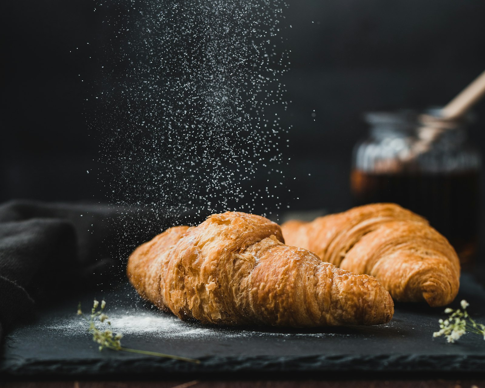 Two croissants on dark slate with icing sugar falling