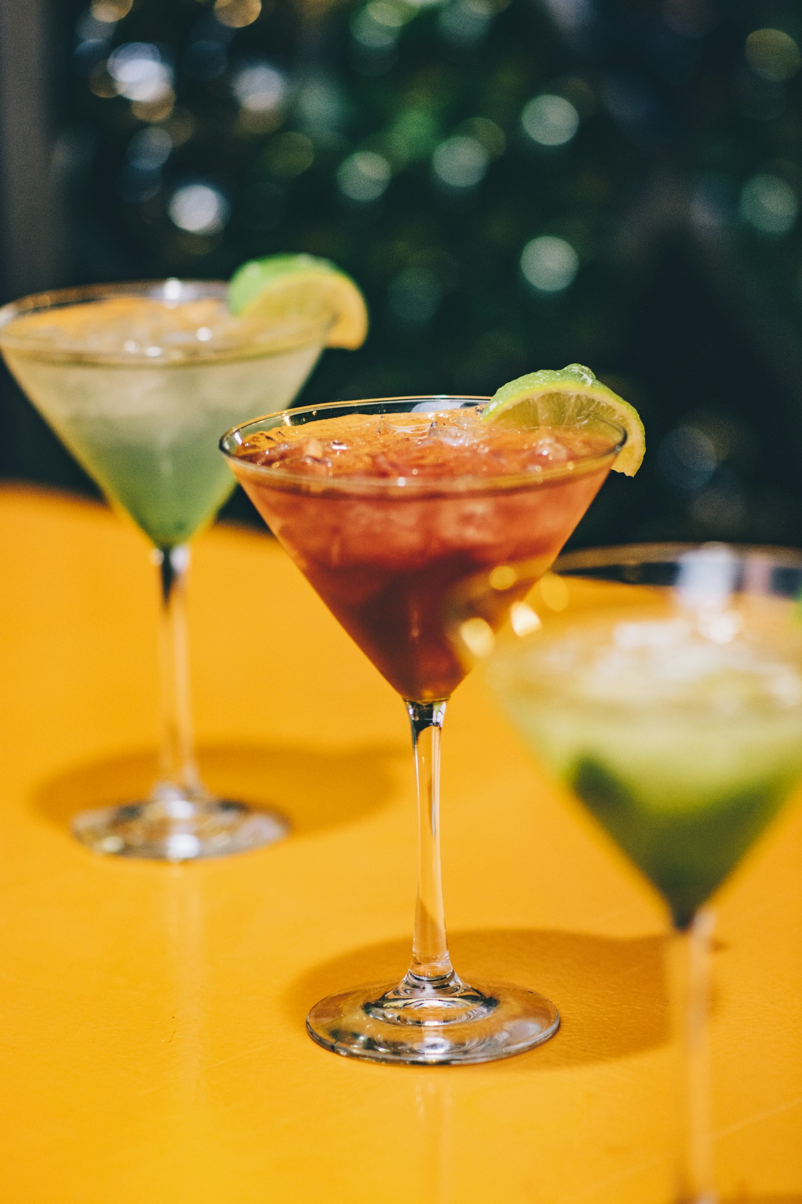 Three neon dessert cocktails lined up on the yellow table
