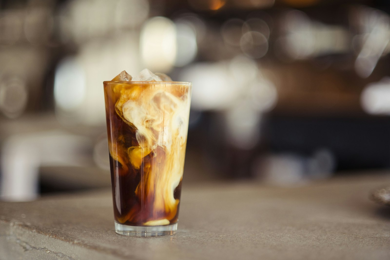 Iced coffee swirling in a tall glass against golden bokeh