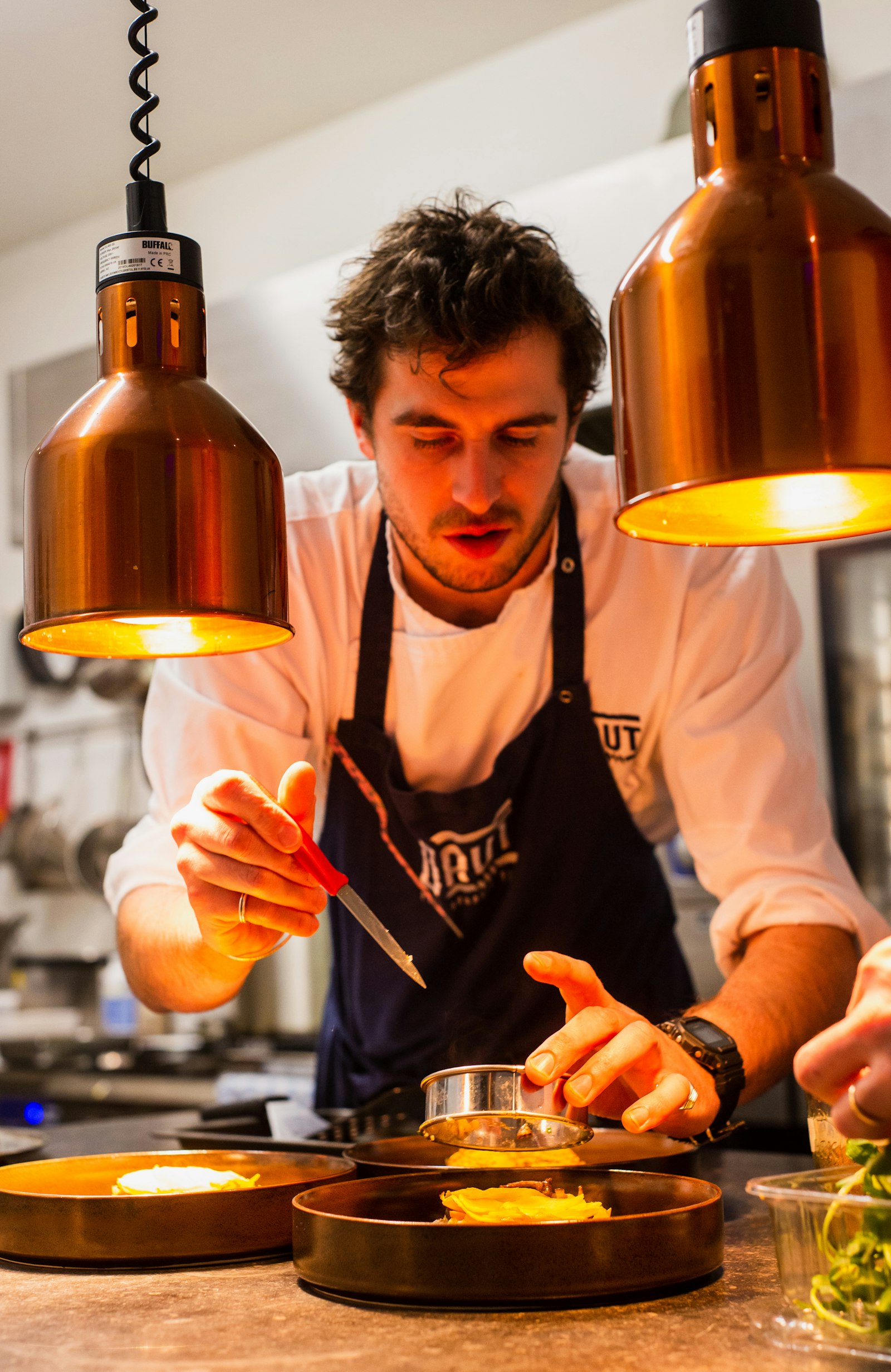 Chef plating desserts under warm copper heat lamps