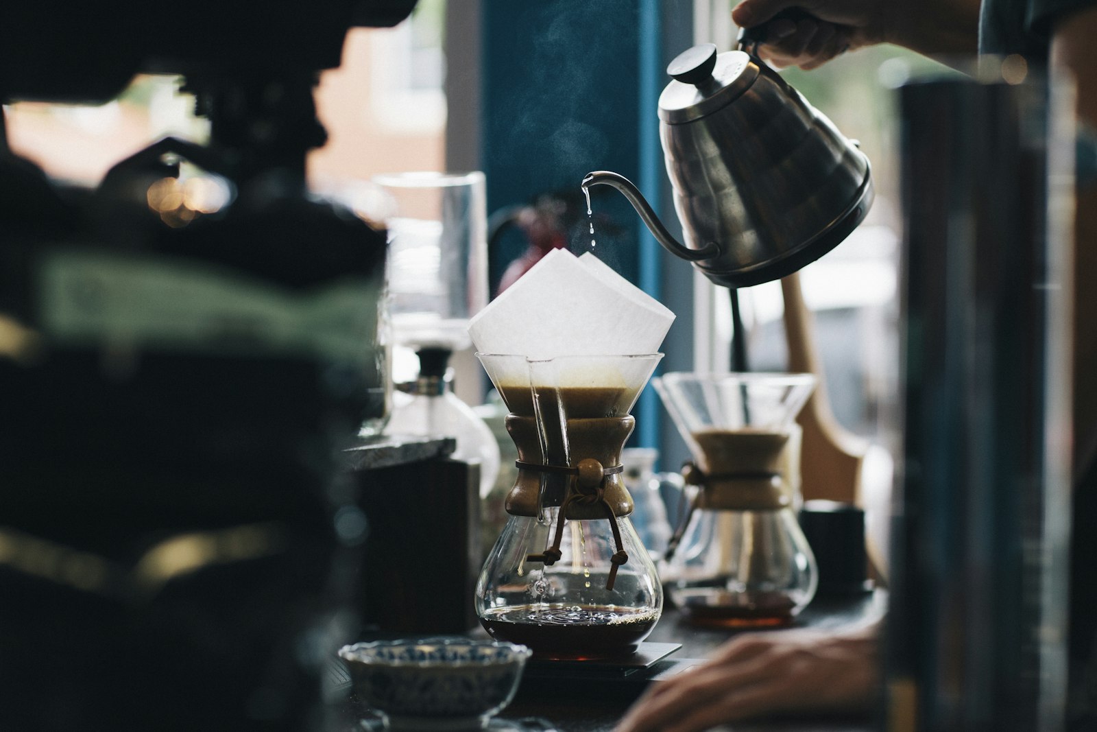 Barista pouring a slow kettle over a Chemex pour-over at the window counter