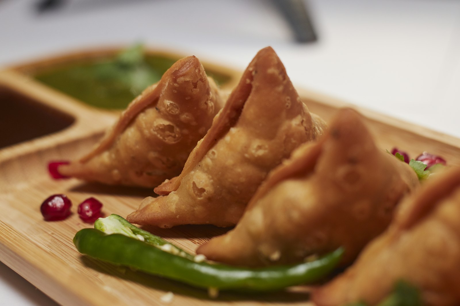 Samosas on a bamboo tray with green chutney and pomegranate pearls